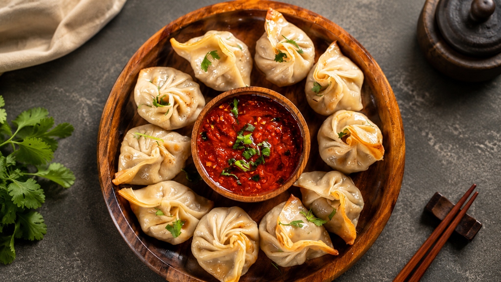 Handcrafted artisan steamed momos arranged in a wooden dish with chili sauce